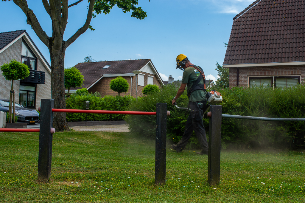 Groenmedewerker aan het bosmaaien op een speelplaats